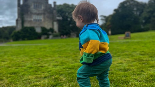 A toddler in brightly coloured jumper and trousers faces away from the camera. The Abbey is visible in the background.